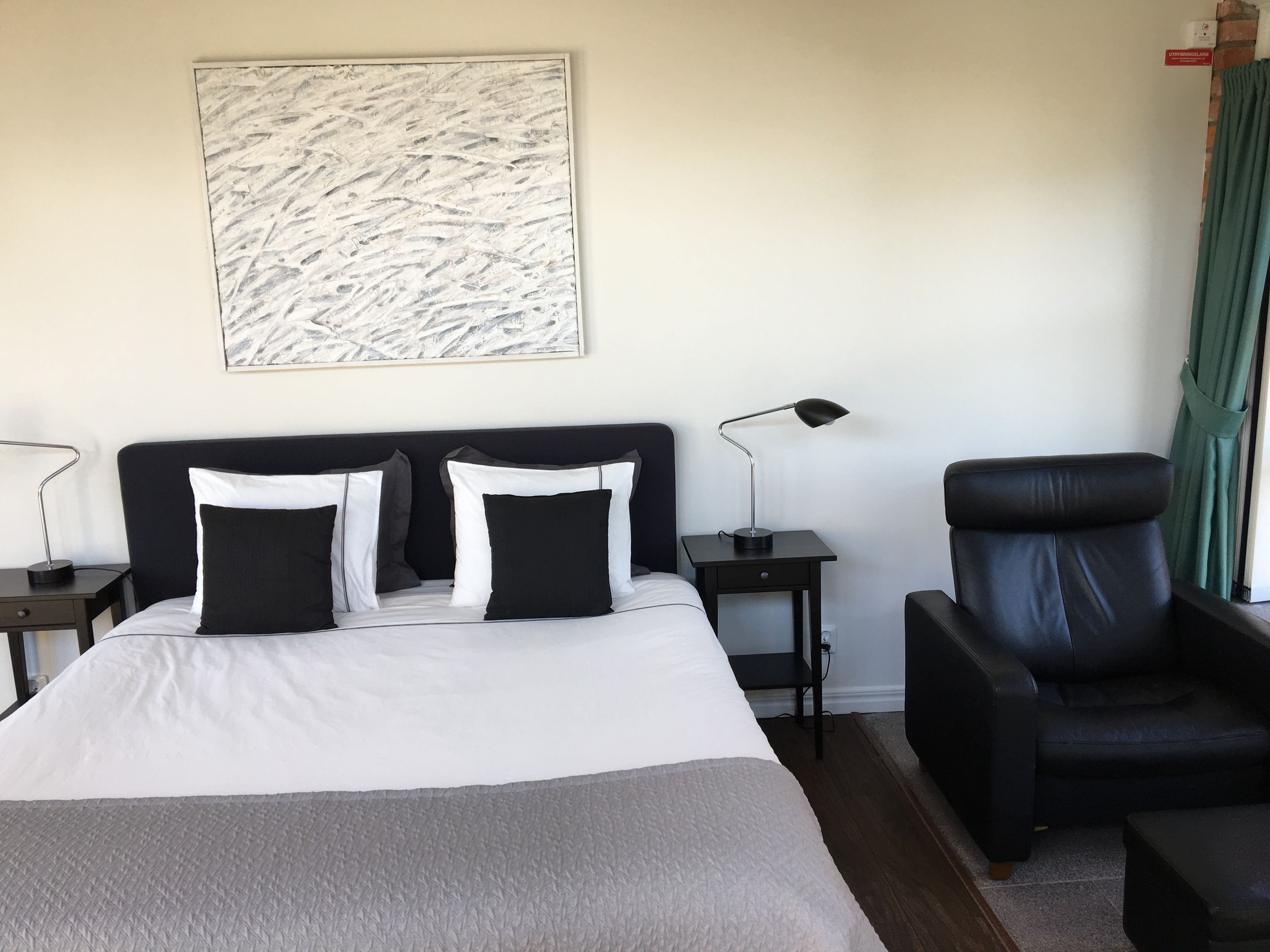 Una habitación de hotel con cama, escritorio, silla y un cuadro en la pared.