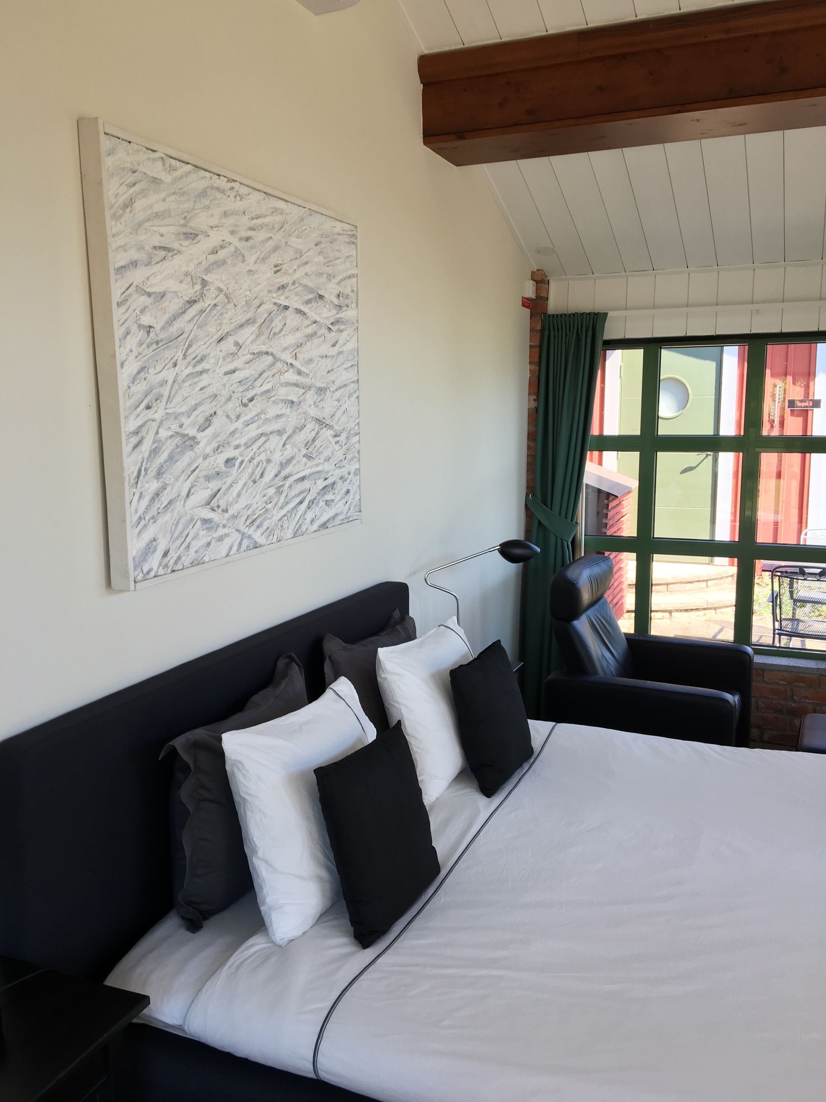 Ein Hotelzimmer mit einem großen Bett, einer Kopfteil, einem Fenster mit Vorhängen und Blick nach außen.