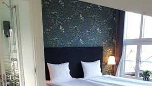 Une chambre moderne avec un grand lit, une porte en verre donnant sur une douche et une vue sur l’extérieur.