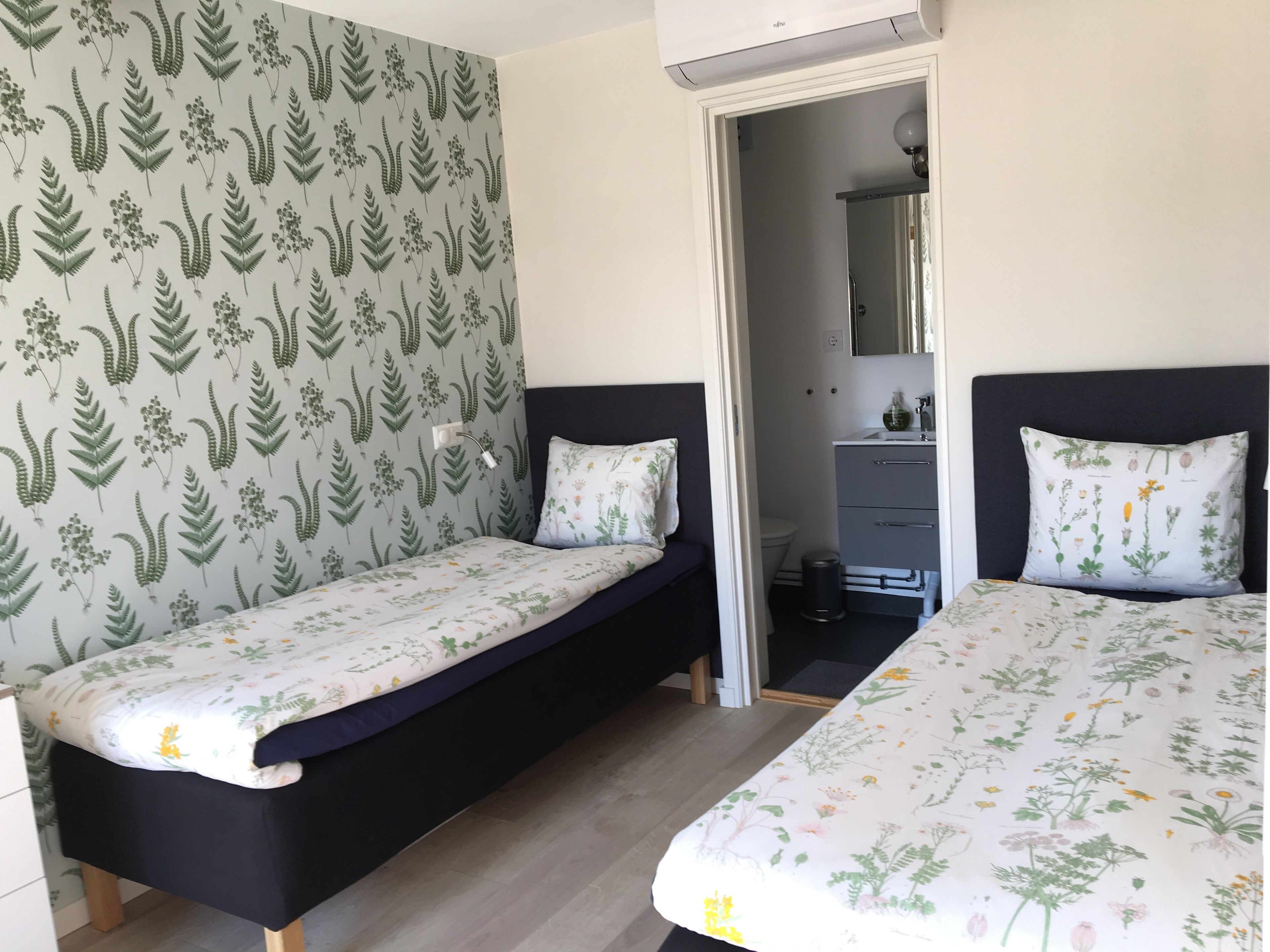 Habitación con dos camas, un escritorio pequeño y un baño visible a través de una puerta abierta.