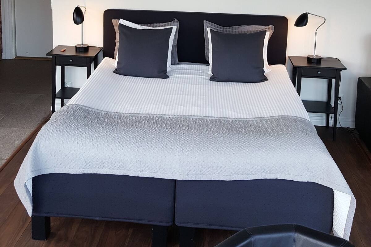 Un dormitorio con una cama grande, dos mesitas de noche, un lámpara en el techo y una obra de arte colgada en la pared.