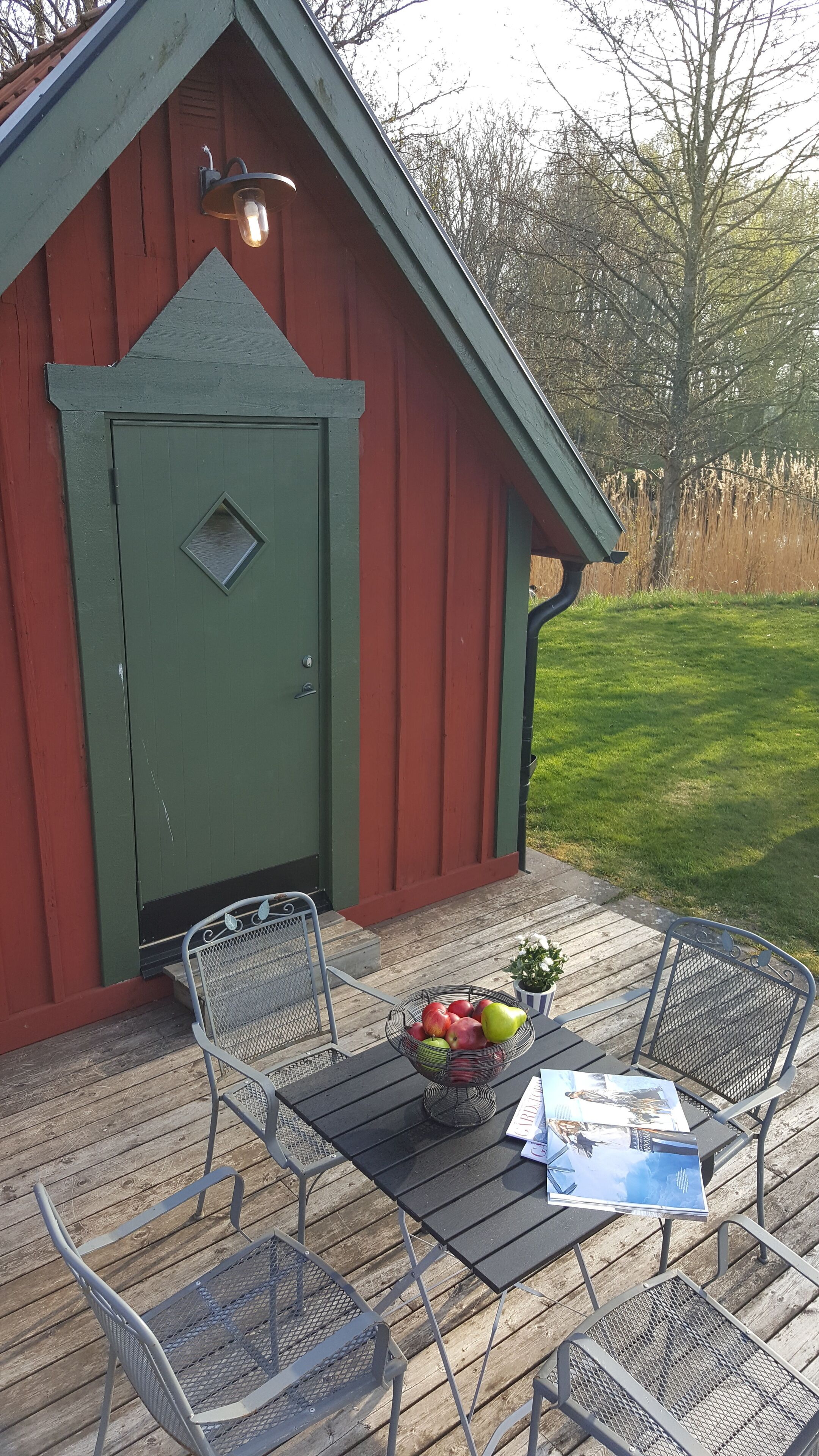 A wooden deck with metal chairs and a table, a small shed with a green door, and a bowl of fruit on the table.