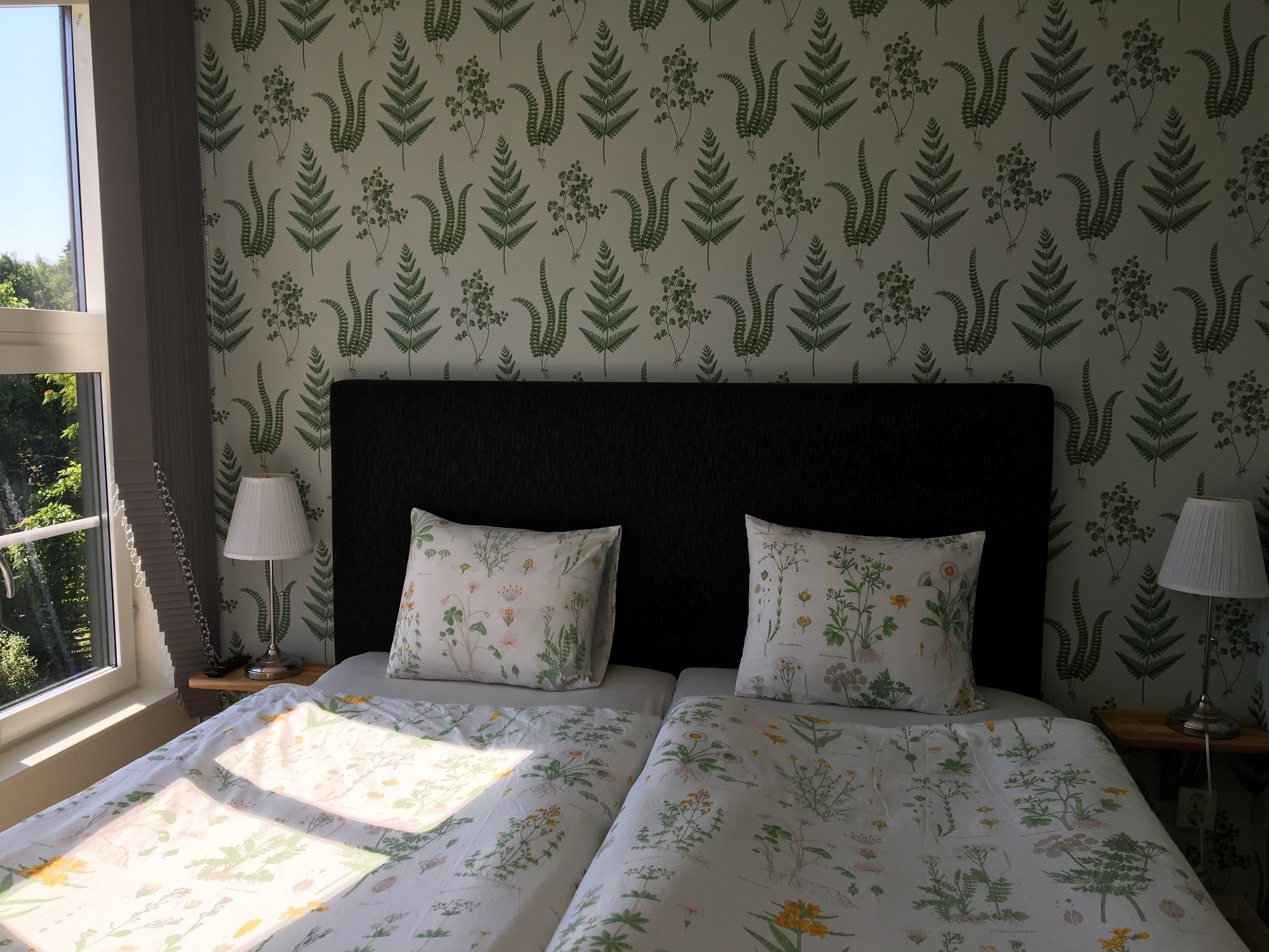 A bedroom with a large bed, two bedside lamps, and a window with a view of greenery.