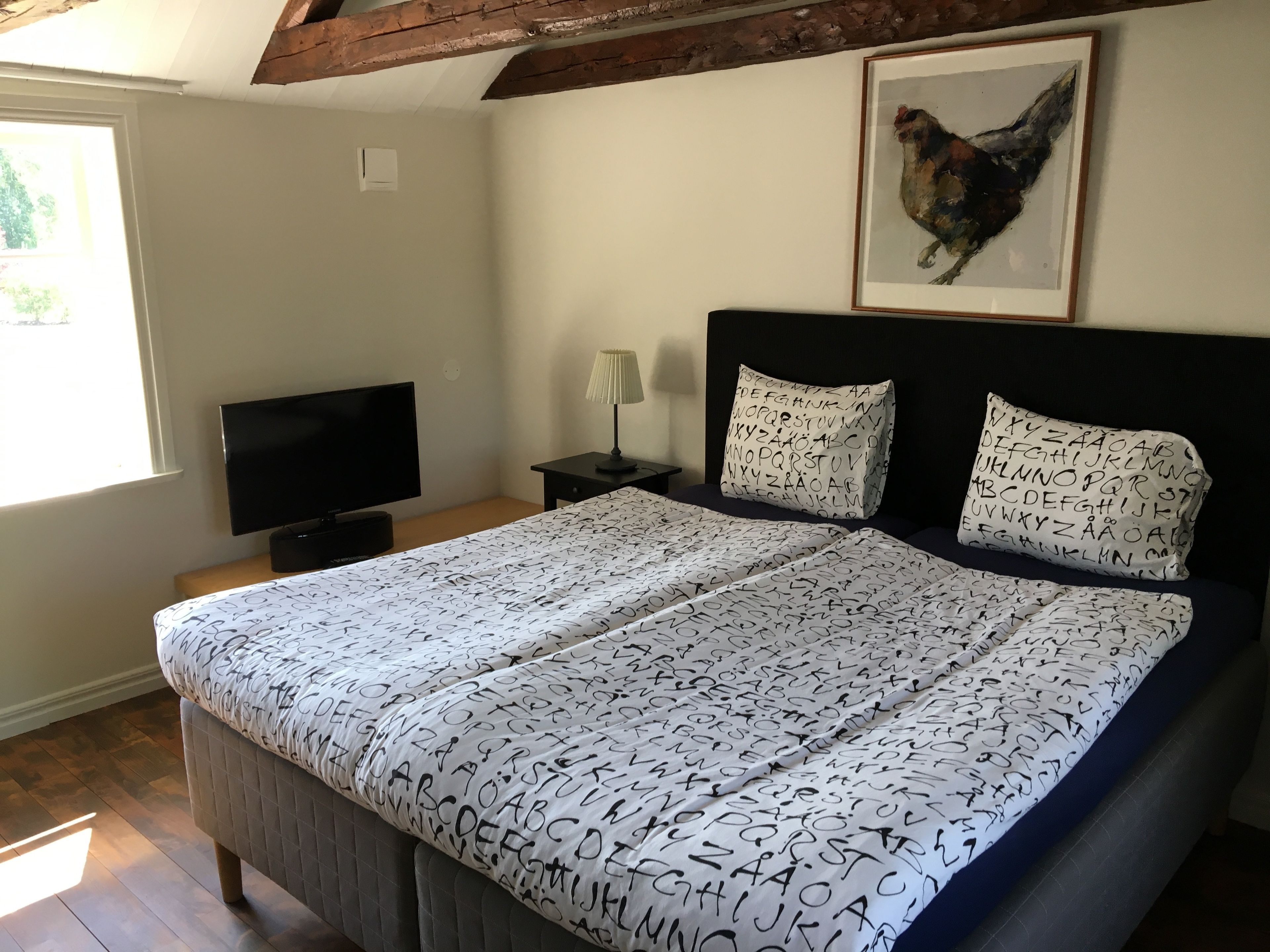 Een slaapkamer met een bed, een televisie, een nachtkastje, een lamp en een lijst met een afbeelding aan de muur.