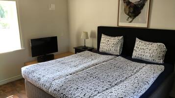 Een slaapkamer met een bed, een televisie, een nachtkastje, een lamp en een lijst met een afbeelding aan de muur.