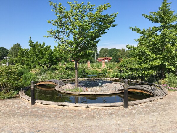 A circular water feature with a bridge, surrounded by greenery and a stone pathway.