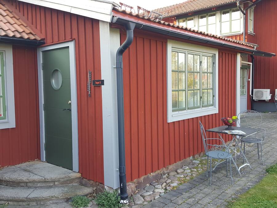 A red building with a green door, a small outdoor seating area with metal chairs and a table, and two air conditioning units on the side.