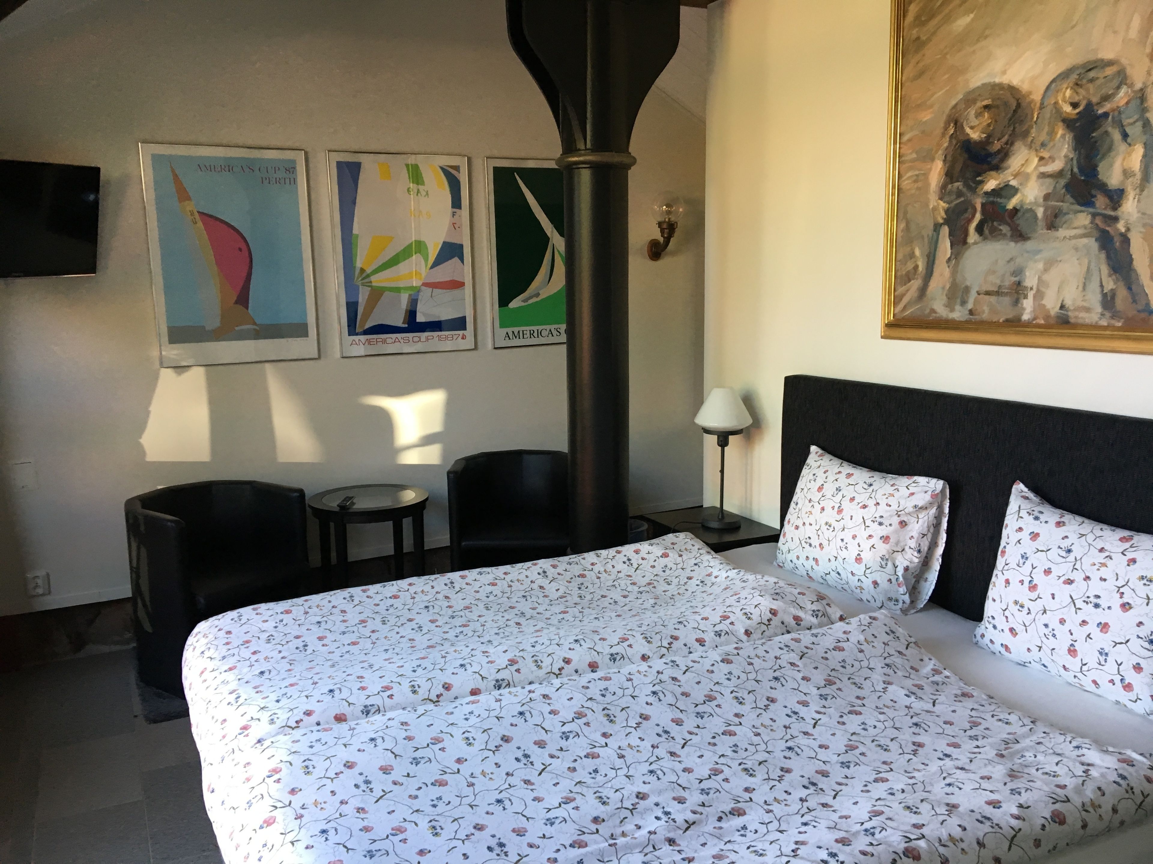 Una habitación de hotel con una cama grande, dos sillas, una mesita y un cuadro en la pared.