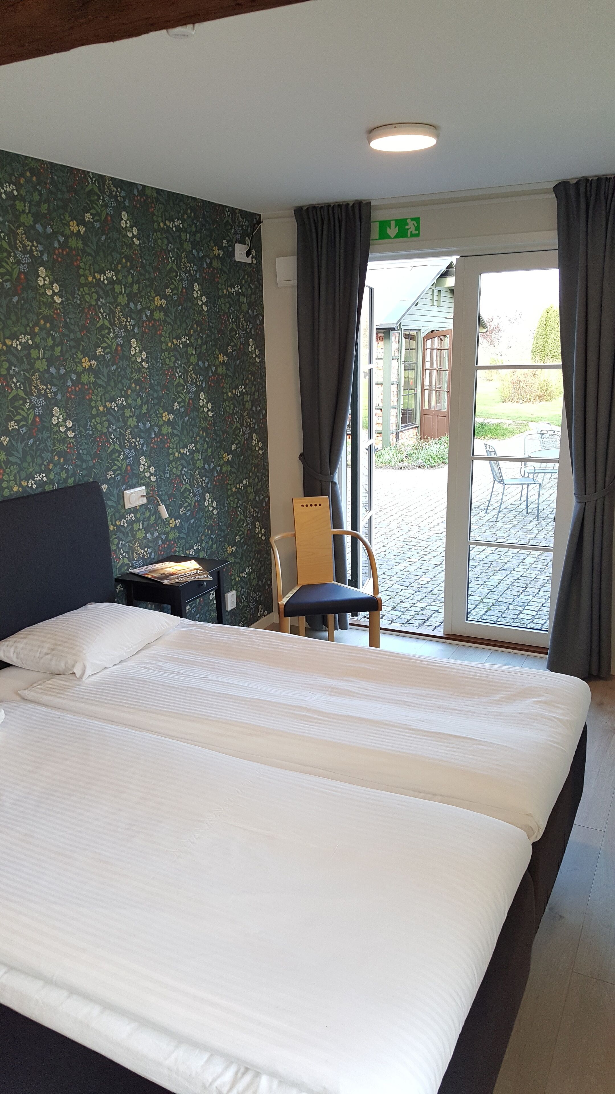 A hotel room with a large bed, a chair, a small table, a lamp, and a view of the outside patio.