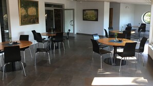 Un vaste espace dédié à la salle à manger, avec de nombreuses tables et chaises, de grands tableaux accrochés aux murs et un design moderne au niveau du plafond.