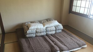 A room with tatami mat flooring, a bed with a quilted mattress and patterned pillows, and a window with a grid pattern. - VOYAN Resort FUJIYAMANAKAKO GEKKOSO (Yamanakako)