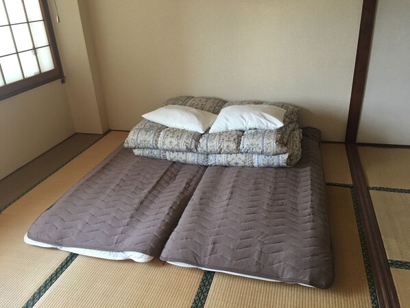 Una habitación con estera de tatami, una cama baja y dos almohadas.