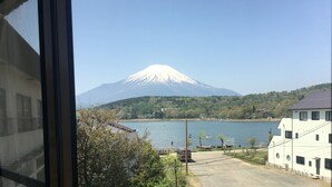 A view of Mount Fuji from a window overlooking a body of water with a small boat and a bus in the foreground. - VOYAN Resort FUJIYAMANAKAKO GEKKOSO (Yamanakako)