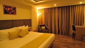Quarto de hotel com uma cama grande, uma escrivaninha, uma cadeira e um quadro na parede.