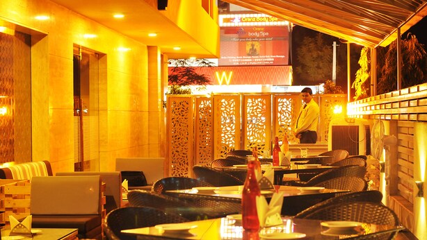 Um restaurante em ambiente interno com móveis de vime, um menu visível e uma pessoa atrás do balcão.