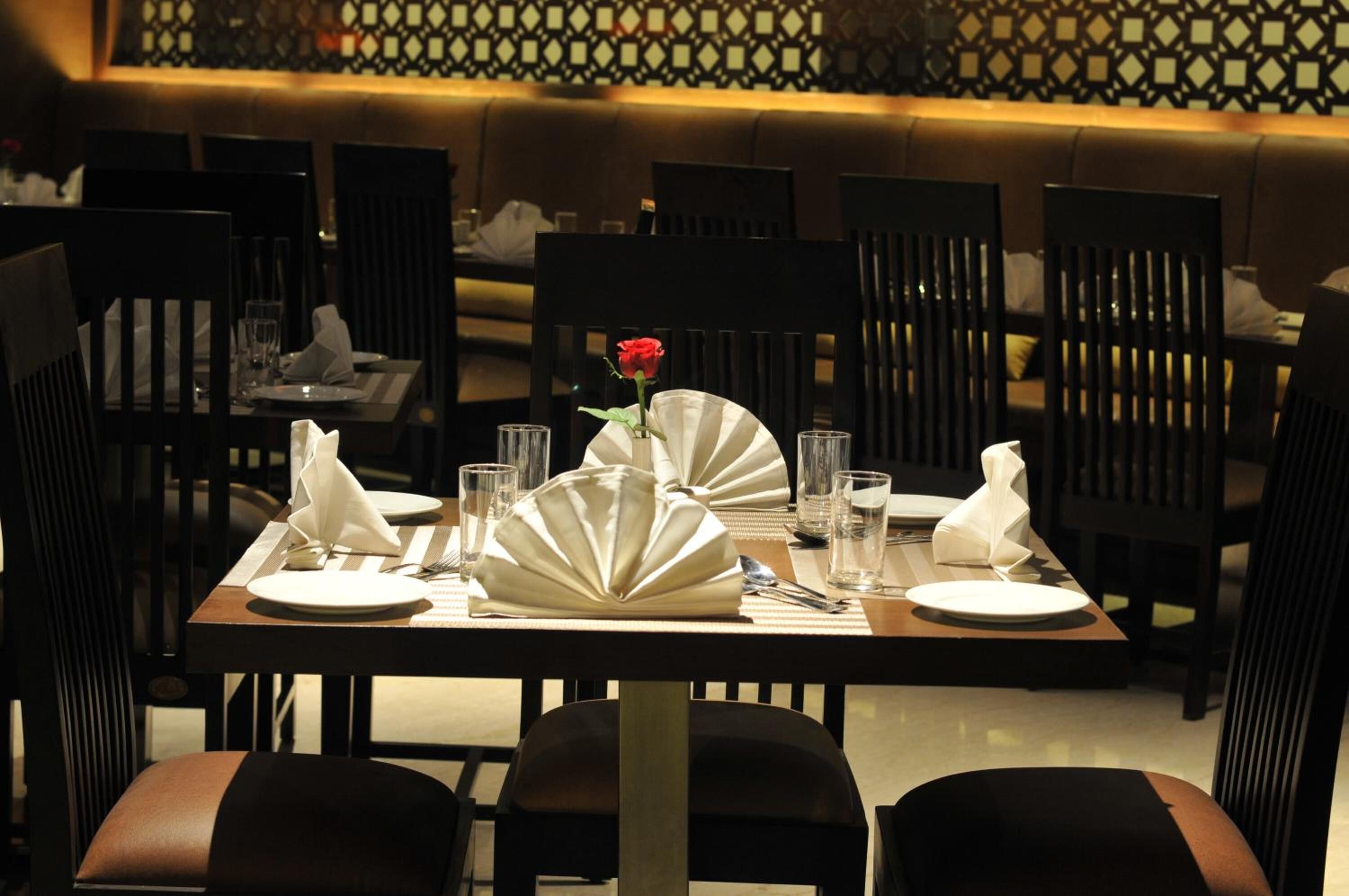 A dining table set with plates, napkins, and a vase with a single red rose.