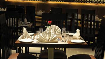 A dining table set with plates, napkins, and a vase with a single red rose.