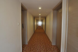 Um corredor de hotel com piso carpete, portas em ambos os lados e um sinal de saída de incêndio na parede direita.