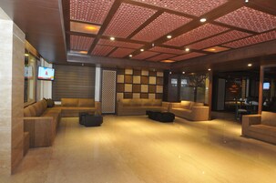 Um hall amplo com design moderno, apresentando um sofá modular, uma mesa de centro e uma parede decorativa com padrão geométrico.