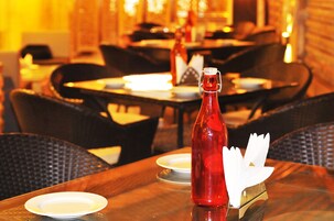 Um ambiente de restaurante com mesas e cadeiras, uma garrafa vermelha e guardanapos brancos sobre uma mesa.
