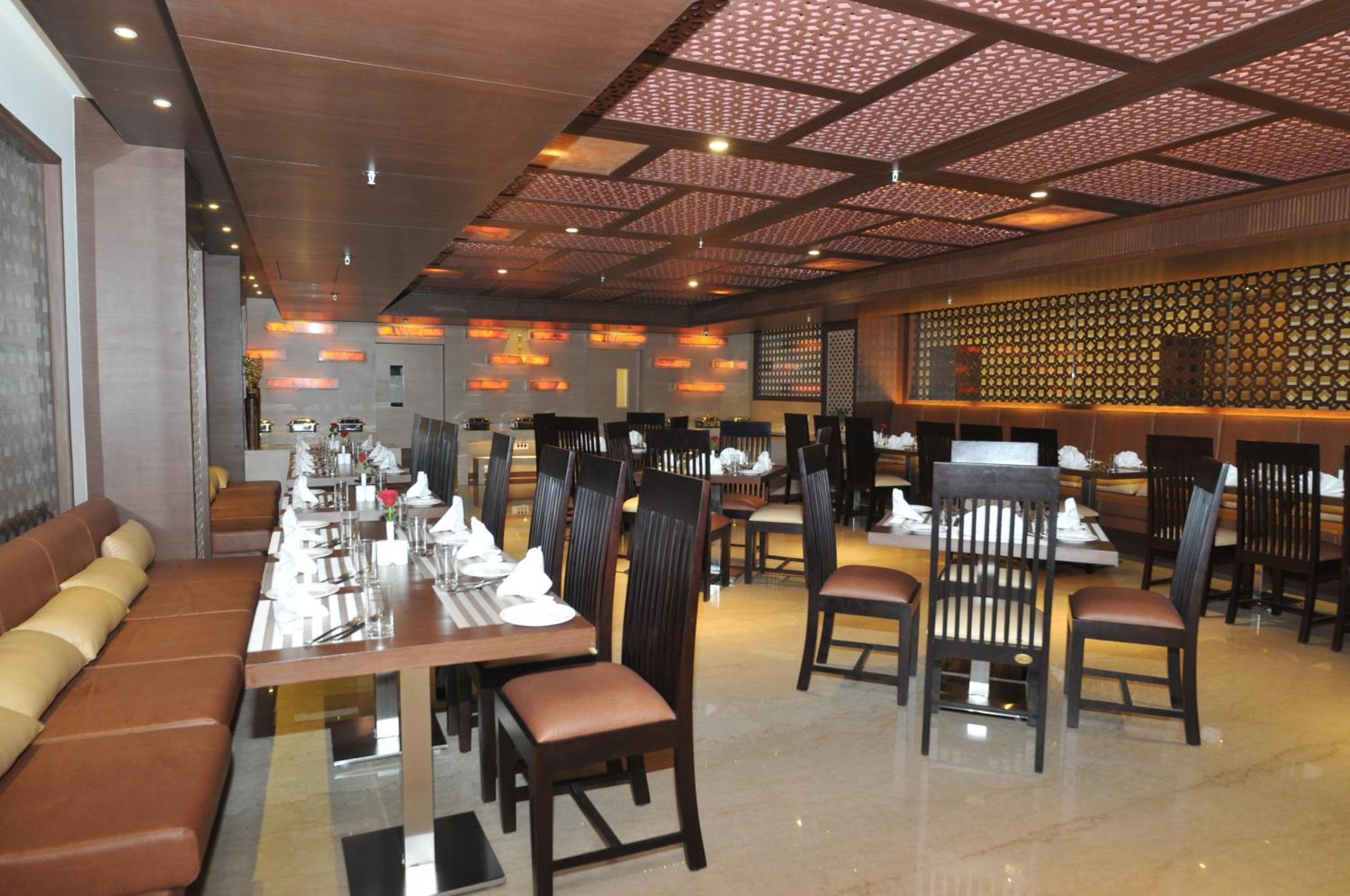 A restaurant with multiple dining tables and booths, a patterned ceiling, and a decorative wall.