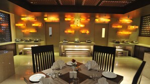 Uma sala de jantar com uma mesa posta para quatro pessoas, rodeada por cadeiras, e iluminada por luzes fixadas na parede.