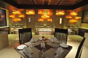 Uma sala de jantar com uma mesa posta para quatro pessoas, rodeada por cadeiras, e iluminada por luzes fixadas na parede.