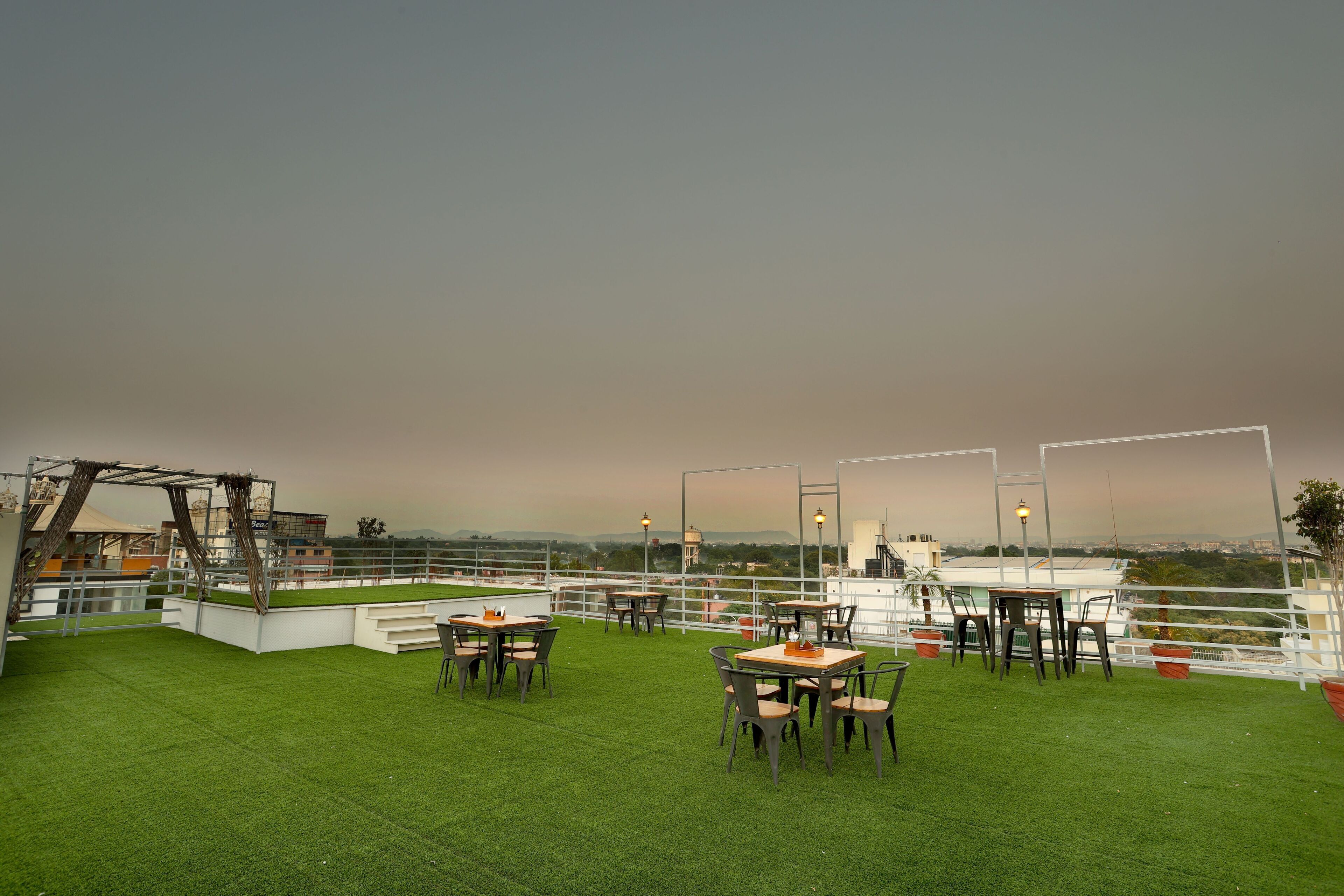 A rooftop terrace with tables and chairs, a view of the city, and a railing.