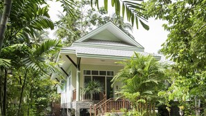 Ein Haus mit Veranda, umgeben von üppiger Vegetation und Palmen.