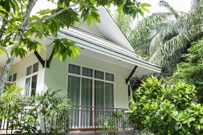 A house with a balcony, surrounded by lush greenery and palm trees.