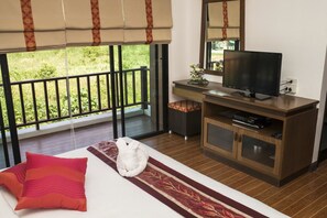 Habitación de hotel con cama, televisión, escritorio pequeño y balcón con vistas a zonas verdes.