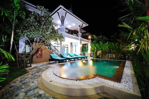 Una casa de dos pisos con piscina, rodeada de plantas tropicales.