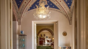 Un gran pasillo con una araña, un arco de entrada a un comedor y una vitrina con objetos.