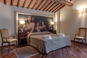 Un dormitorio con una cama grande, dos sillas, una mesita de noche, un cuadro en la pared y un techo de madera.