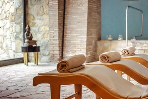 A spa room with wooden loungers, a stone wall, and a small statue. - Campomaggio (Radda in Chianti)