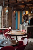 Interior de restaurante con mesas redondas, sillas rojas y una zona de bar con estantes llenos de botellas.
