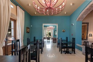 Comedor con pared verde azulado, sillas negras y una lámpara de araña en el centro.