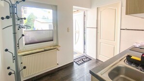 Une cuisine avec un radiateur, une fenêtre équipée de stores, une porte et un paillasson.