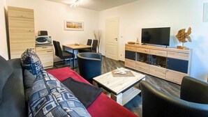 Un salon moderne comprenant un canapé, une table à manger, des chaises, un téléviseur et un meuble.