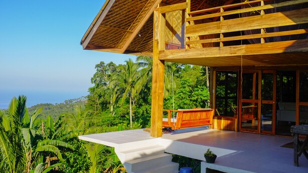 Une structure en bois dotée d’un balcon donnant sur une végétation luxuriante et offrant une vue dégagée sur le paysage environnant.