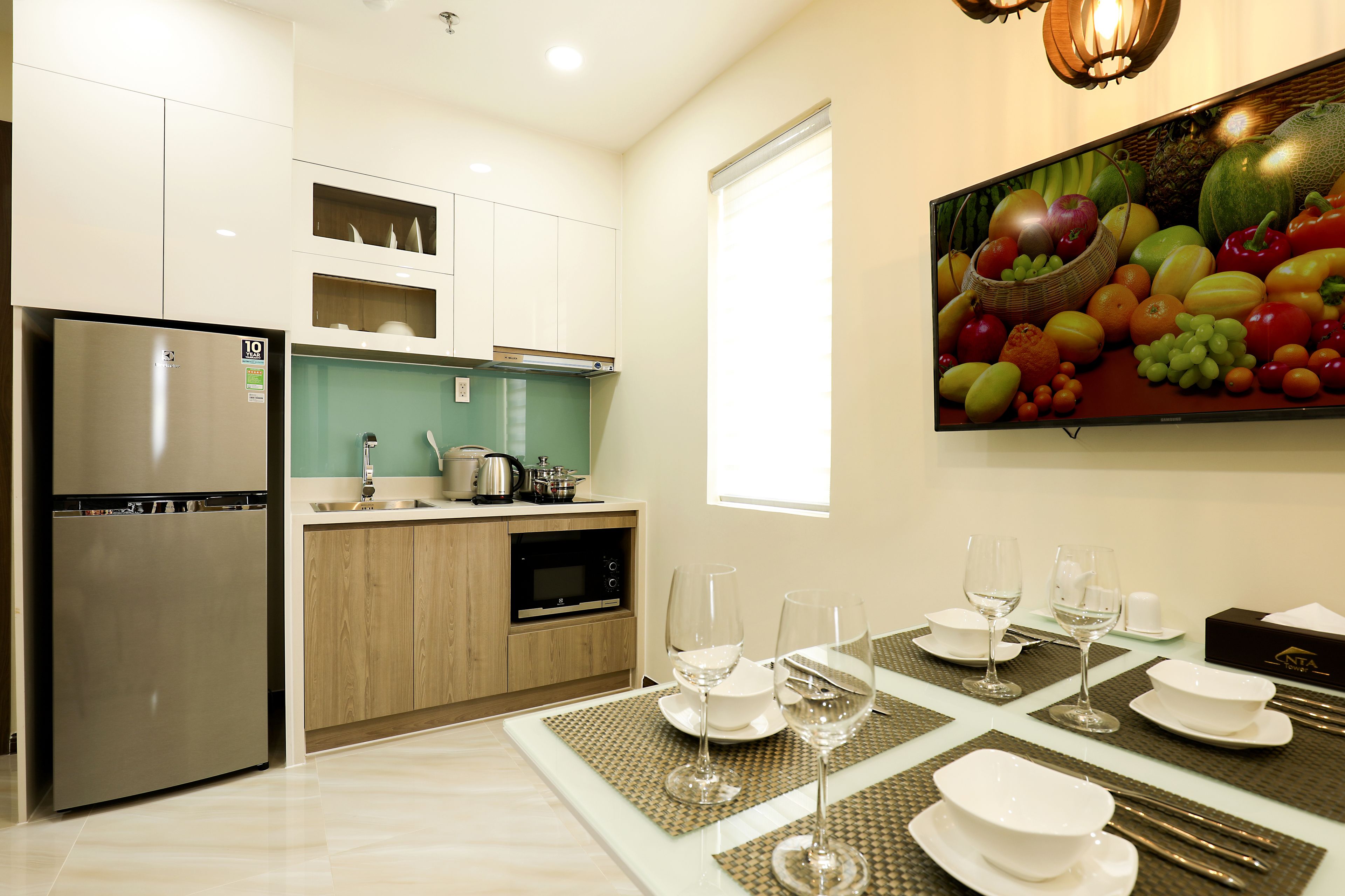 A modern kitchen with a stainless steel refrigerator, wooden cabinets, and a dining area set for a meal with white tableware and wine glasses.