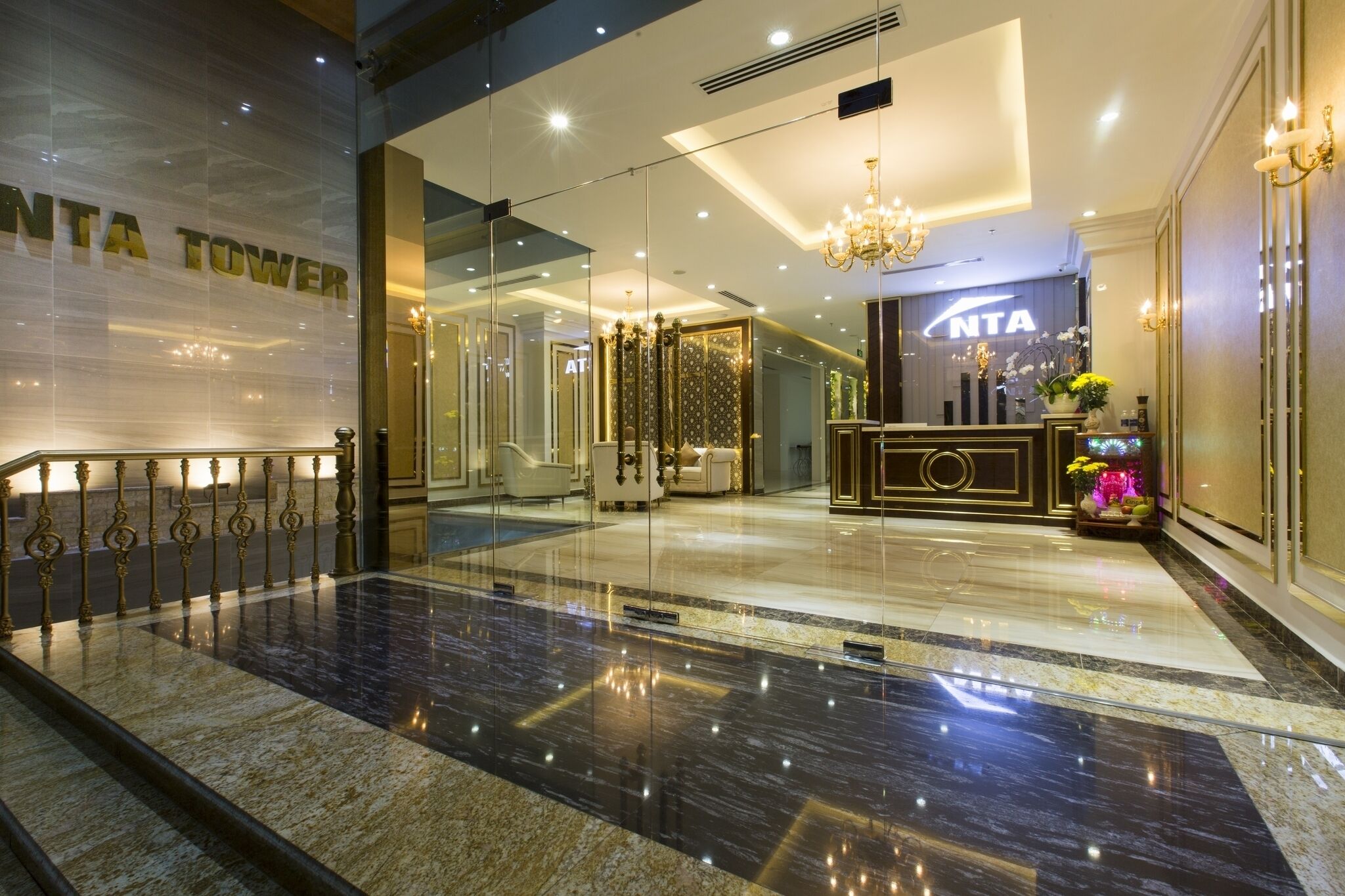 Un hall d’hôtel avec une entrée en verre, un comptoir d’accueil et un lustre.