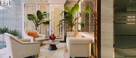 A lobby with two white sofas, a coffee table with red flowers, and large green plants.