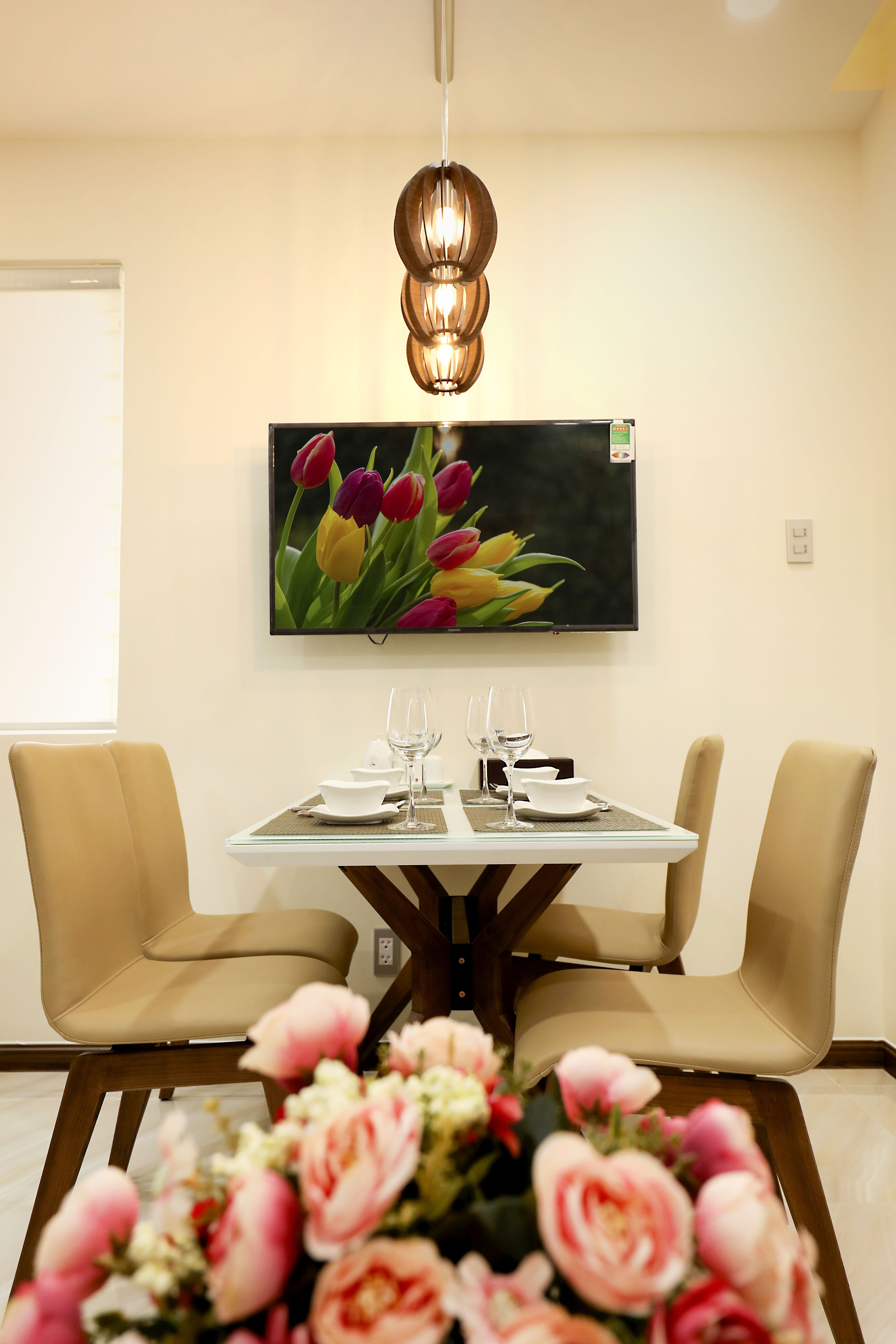 A dining area with a table set for two, a wall-mounted TV, and a floral arrangement on the table.
