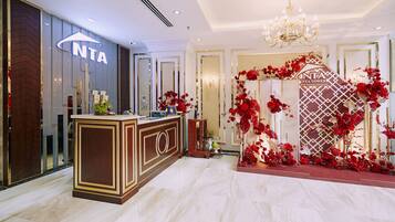 A hotel reception area with a modern design, featuring a reception desk, a chandelier, and red floral decorations.