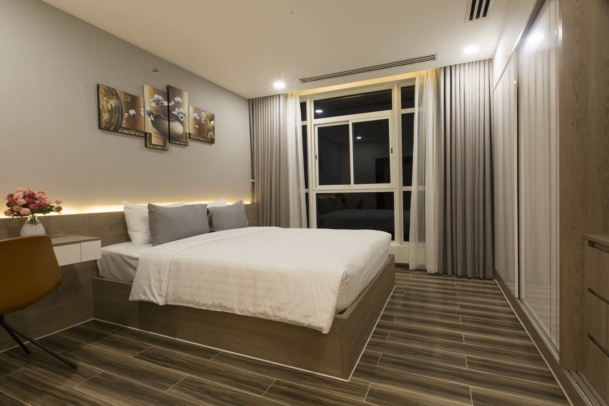 A modern hotel room with a large bed, a desk, and a window with curtains.