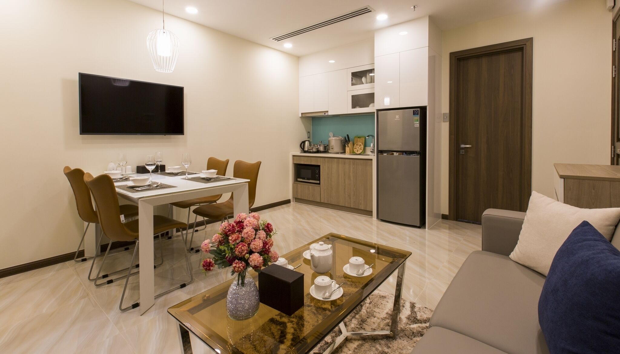 A modern living room with a dining area, a kitchen, and a TV mounted on the wall.