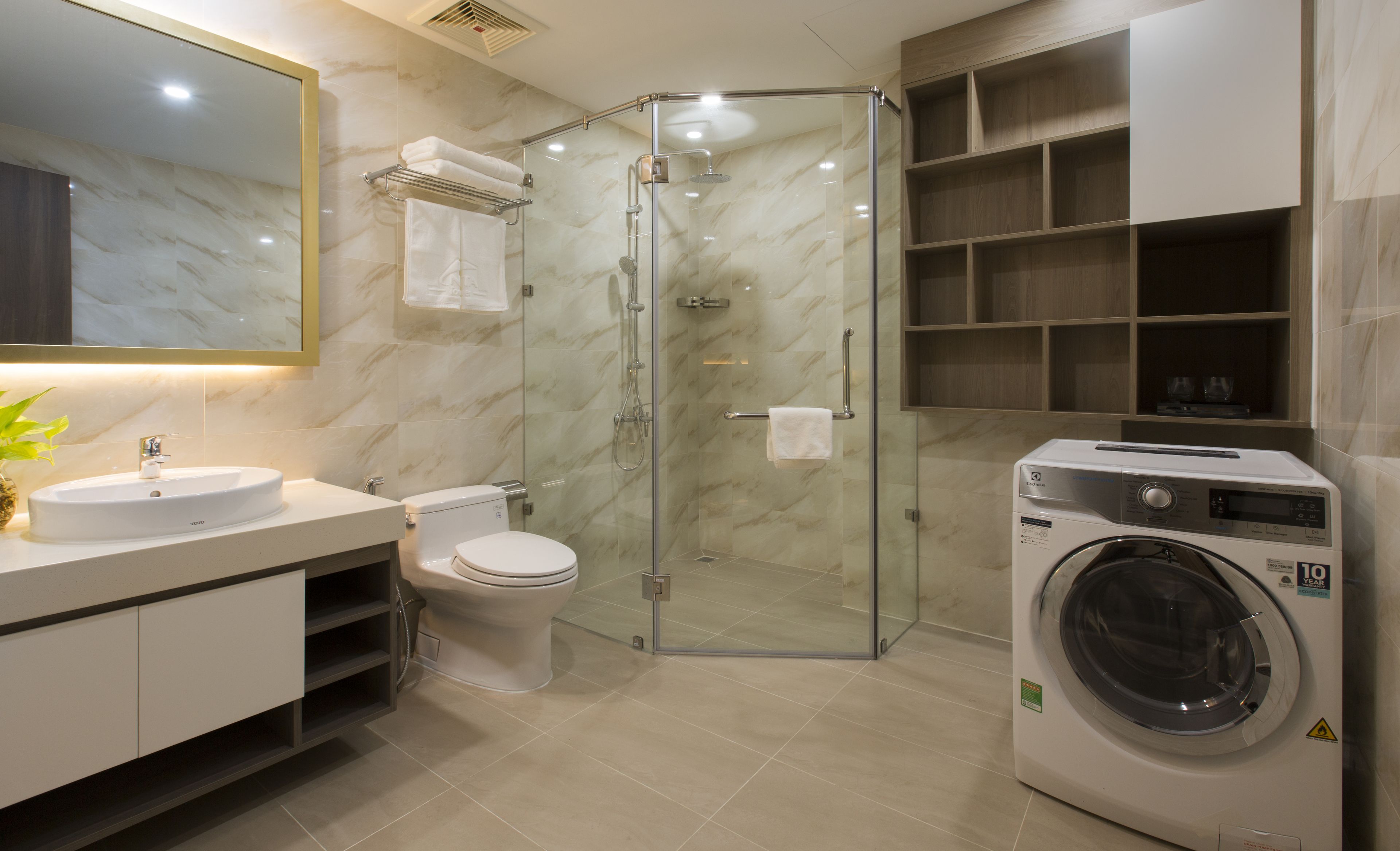 A modern bathroom with a glass-enclosed shower, a toilet, a sink, and a built-in washing machine.