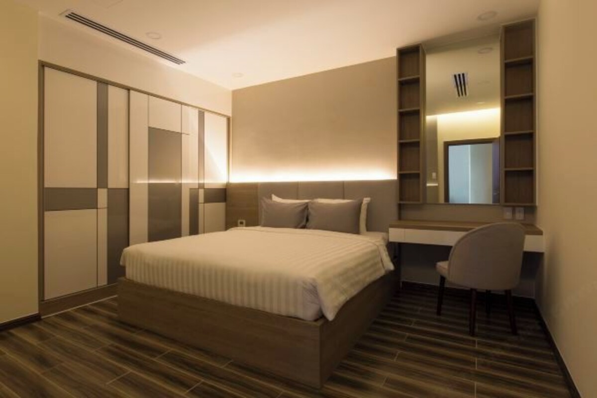 Habitación de hotel moderna con una cama grande, un escritorio y una silla. Se observa un armario y un espejo en la pared.