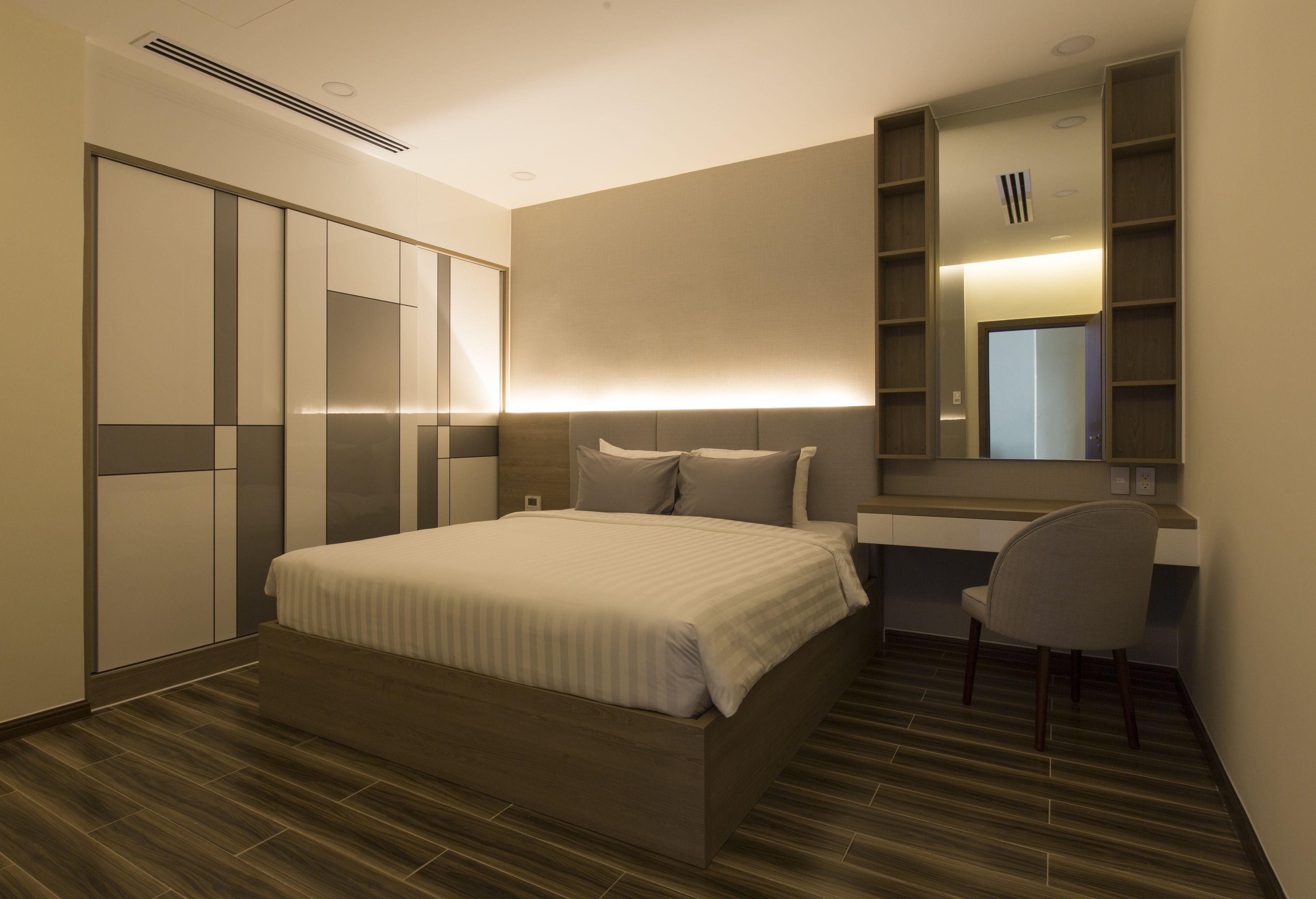 Une chambre d’hôtel moderne avec un grand lit, un bureau et une chaise. On y trouve une armoire avec des portes coulissantes et un miroir au-dessus du bureau.